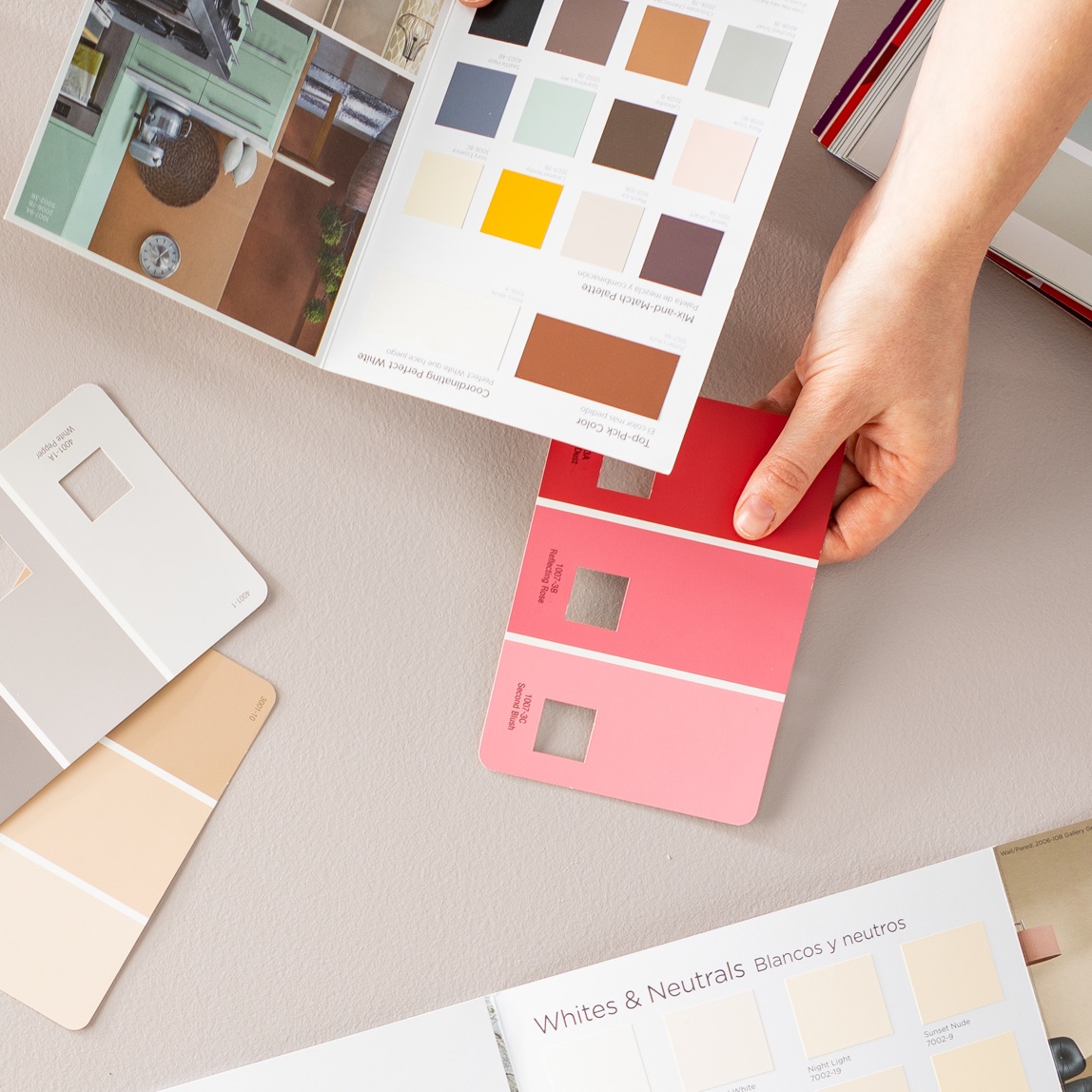 Hand holds color brochure and three-color palette paint chip as if working with a client across the table.